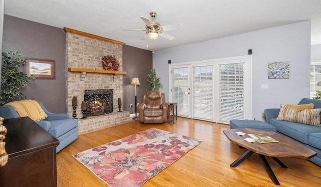 living area featuring a brick fireplace, ceiling fan, and wood finished floors