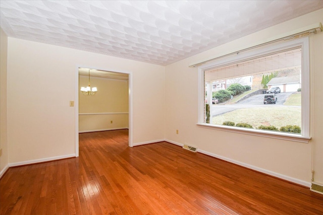 spare room with visible vents, a notable chandelier, baseboards, and hardwood / wood-style flooring