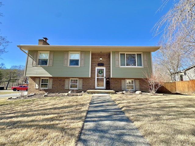 raised ranch with a front yard, brick siding, fence, and a chimney