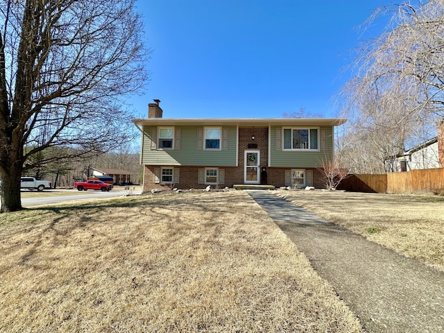 bi-level home featuring brick siding, a chimney, and fence