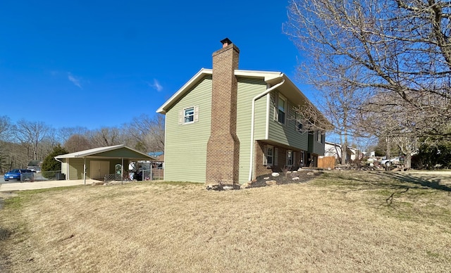 view of side of home featuring a carport, brick siding, a chimney, and a lawn