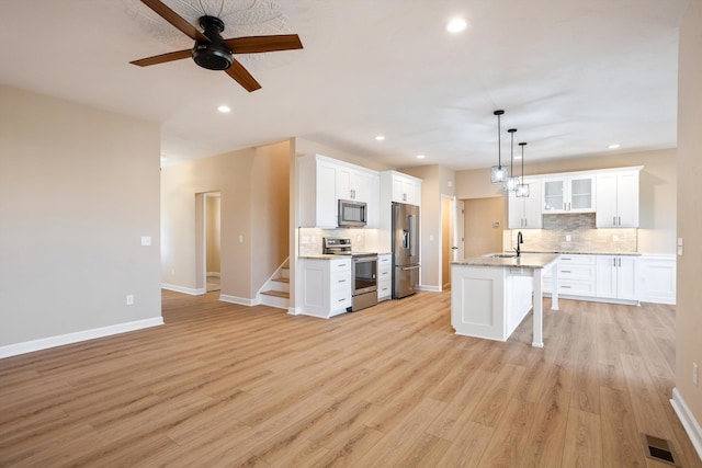 kitchen with stainless steel appliances, visible vents, decorative backsplash, light wood-style floors, and a sink