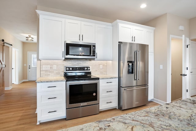 kitchen featuring appliances with stainless steel finishes, a barn door, decorative backsplash, and white cabinets