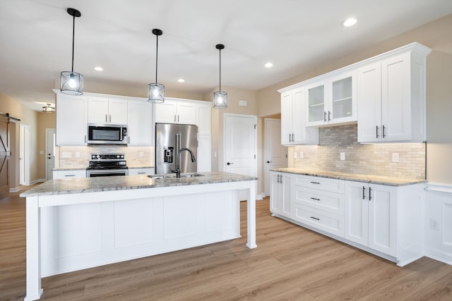 kitchen featuring light wood finished floors, stainless steel appliances, a barn door, white cabinetry, and a sink