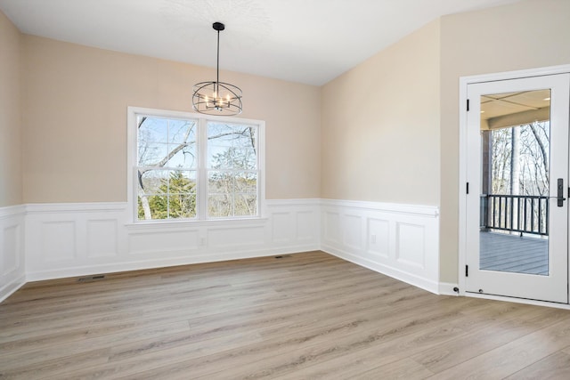 unfurnished dining area with light wood-style floors, a wainscoted wall, visible vents, and an inviting chandelier