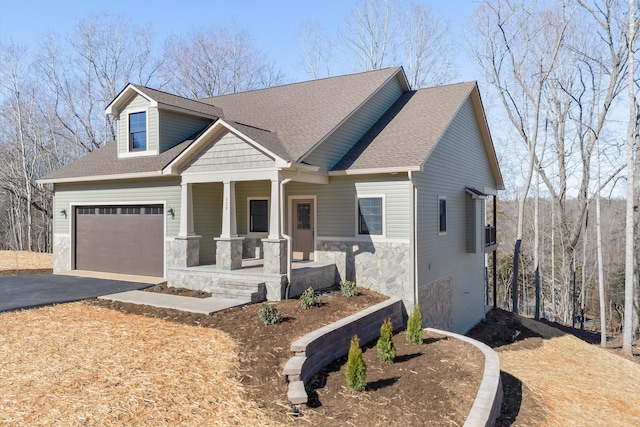 craftsman-style house with stone siding, covered porch, a shingled roof, and aphalt driveway