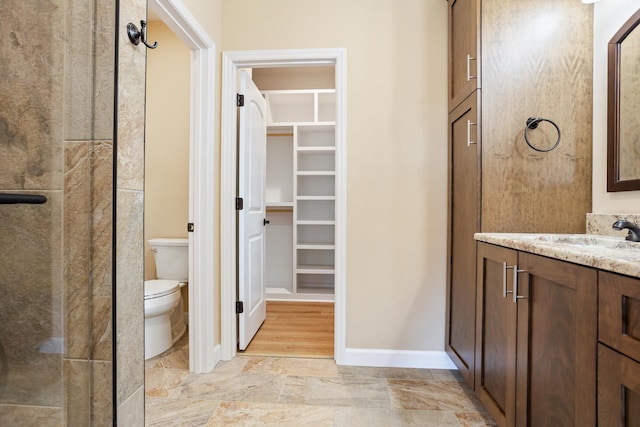 full bathroom featuring a spacious closet, toilet, stone finish floor, vanity, and baseboards