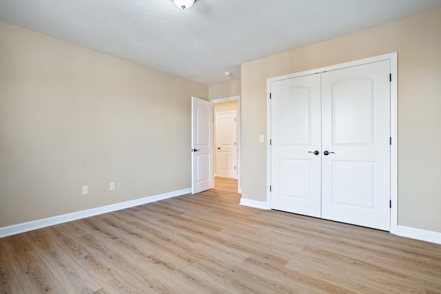 unfurnished bedroom featuring light wood-style floors, baseboards, and a closet