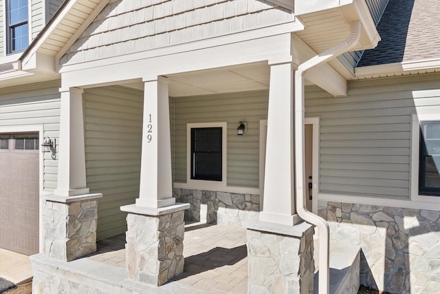 view of exterior entry with covered porch, stone siding, and a shingled roof