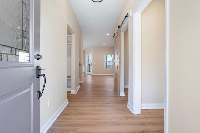 hall with recessed lighting, light wood-style flooring, baseboards, and a barn door