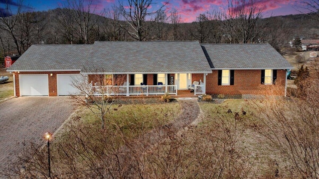 single story home with an attached garage, covered porch, decorative driveway, and brick siding