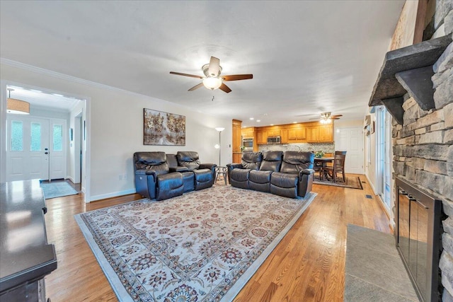 living room with light wood-type flooring, baseboards, ornamental molding, and a ceiling fan