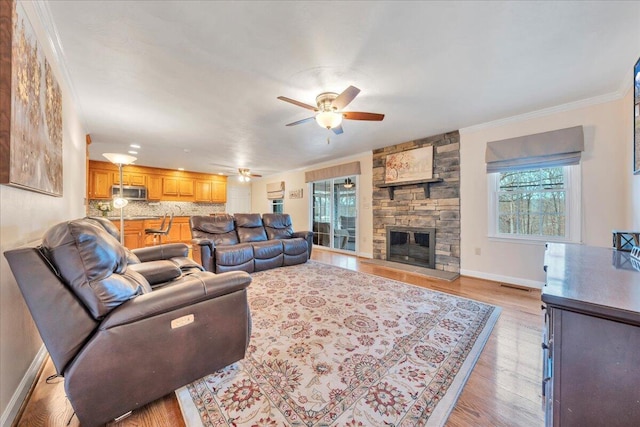 living room featuring plenty of natural light, a fireplace, light wood-style flooring, and crown molding