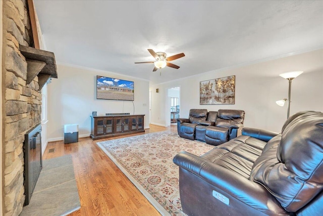 living room featuring a fireplace, a ceiling fan, baseboards, light wood-type flooring, and crown molding