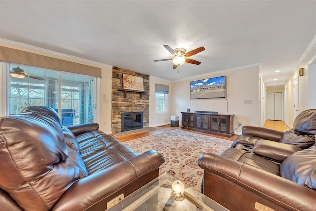 living area with baseboards, a ceiling fan, wood finished floors, crown molding, and a stone fireplace