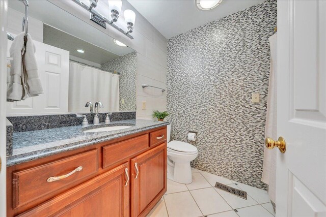 bathroom with toilet, visible vents, vanity, tile walls, and tile patterned floors