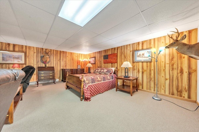 bedroom with carpet floors, a drop ceiling, wood walls, and baseboards