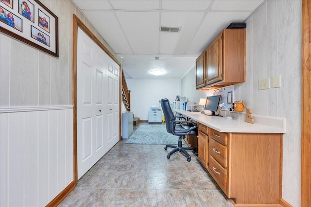 office with built in desk, wood walls, visible vents, and a drop ceiling