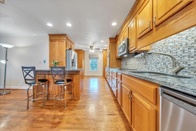 kitchen featuring a breakfast bar, stainless steel appliances, tasteful backsplash, a sink, and dark stone counters