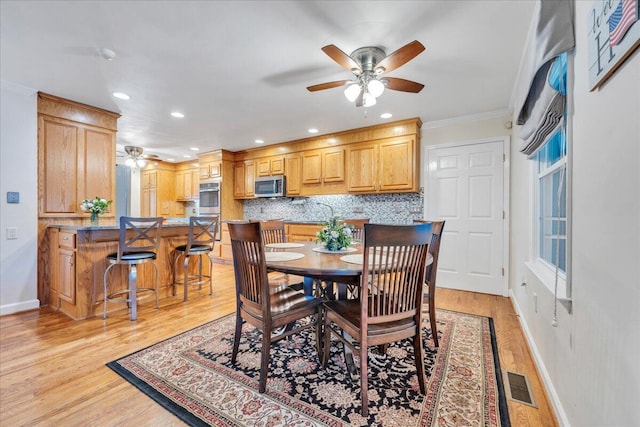 dining room featuring visible vents, baseboards, light wood-style flooring, ceiling fan, and ornamental molding