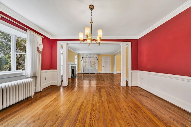 interior space featuring wainscoting, radiator heating unit, wood finished floors, ornate columns, and a fireplace