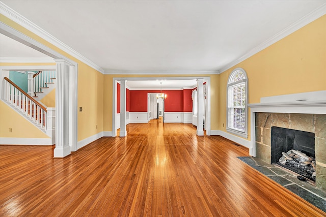 unfurnished living room with decorative columns, a tile fireplace, ornamental molding, wood finished floors, and stairs