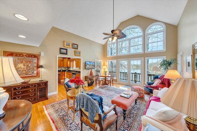 living room featuring baseboards, light wood finished floors, high vaulted ceiling, ceiling fan, and french doors