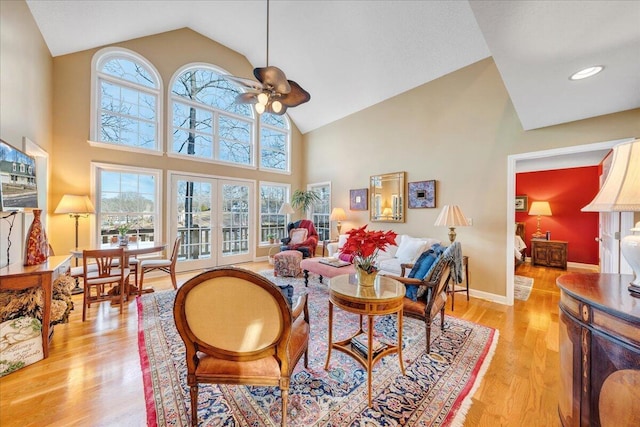 living area featuring light wood finished floors, baseboards, french doors, high vaulted ceiling, and a ceiling fan