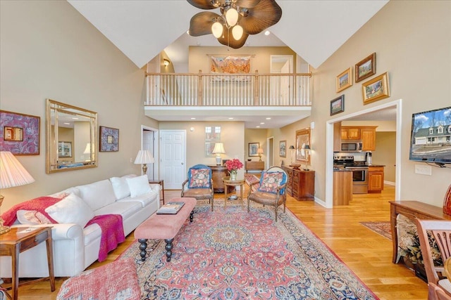 living area featuring a ceiling fan, light wood-style floors, baseboards, and a towering ceiling