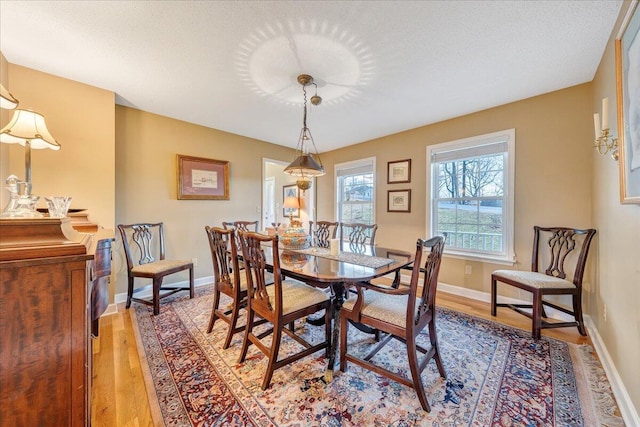 dining space featuring light wood-style flooring, a textured ceiling, and baseboards