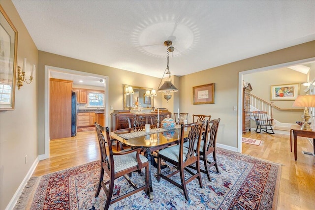 dining area with light wood-type flooring, baseboards, and stairs