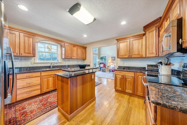 kitchen featuring dark stone countertops, light wood-type flooring, appliances with stainless steel finishes, and decorative backsplash