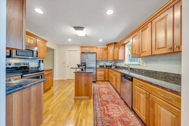 kitchen featuring light wood finished floors, decorative backsplash, dark stone countertops, and appliances with stainless steel finishes