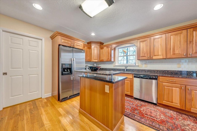 kitchen featuring dark stone countertops, a center island, light wood-type flooring, and stainless steel appliances