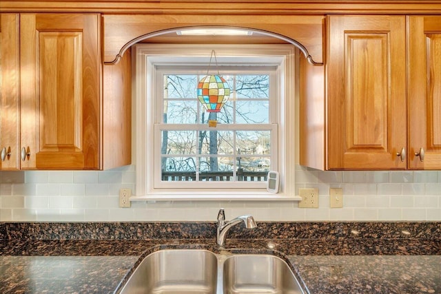 details with tasteful backsplash, dark stone countertops, brown cabinets, and a sink