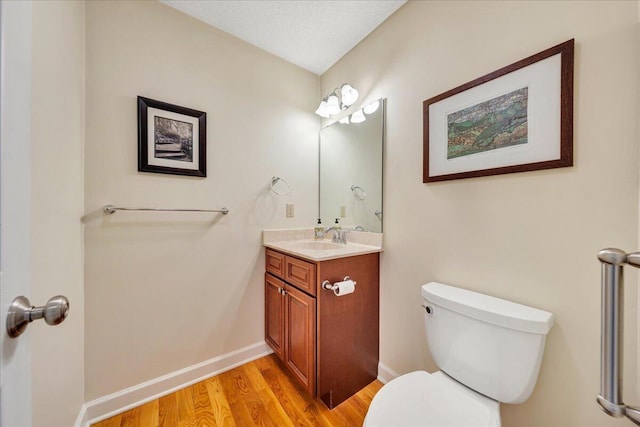 half bathroom featuring toilet, a textured ceiling, wood finished floors, baseboards, and vanity