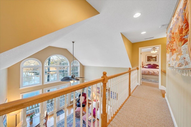 corridor with visible vents, baseboards, light colored carpet, lofted ceiling, and a textured ceiling