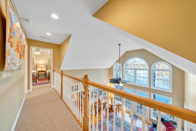 corridor featuring visible vents, a textured ceiling, carpet floors, baseboards, and vaulted ceiling