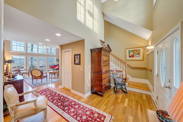 entrance foyer featuring baseboards, a towering ceiling, stairs, and light wood finished floors