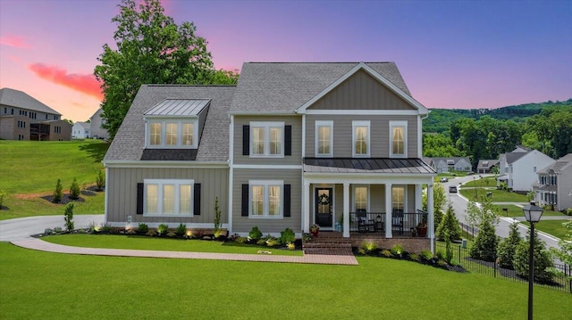 view of front of home with metal roof, a porch, a lawn, board and batten siding, and a standing seam roof