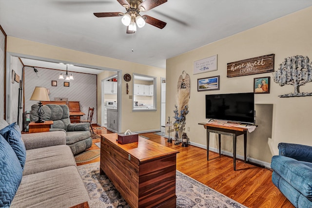 living area with ceiling fan with notable chandelier, baseboards, and wood finished floors