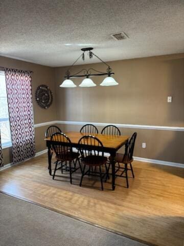 dining space featuring a textured ceiling, wood finished floors, and visible vents