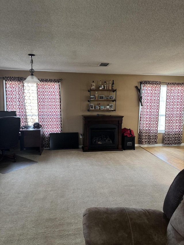 living room with a fireplace, visible vents, carpet flooring, a textured ceiling, and baseboards