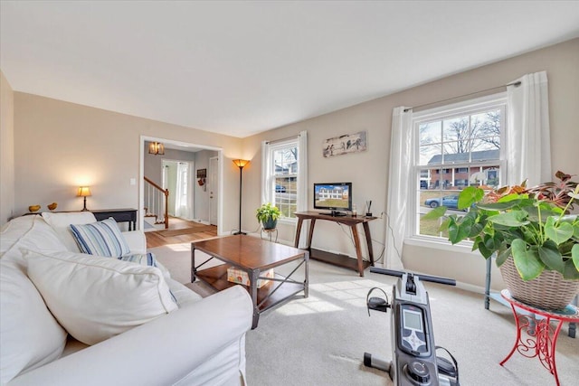 living area featuring light carpet, baseboards, and stairway