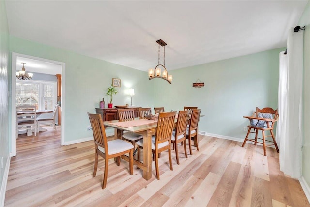 dining room with light wood-type flooring, baseboards, and an inviting chandelier