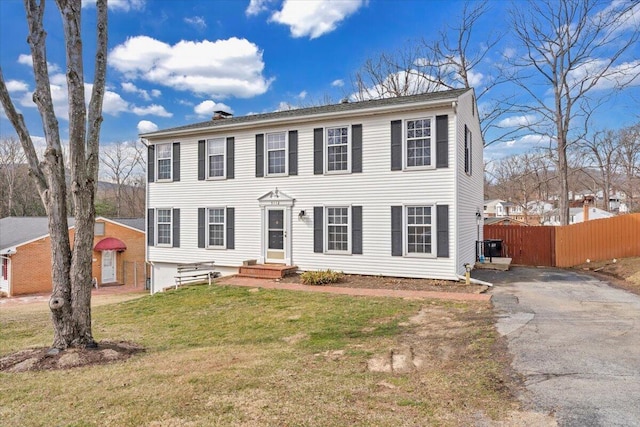 colonial-style house featuring entry steps, fence, driveway, and a front lawn