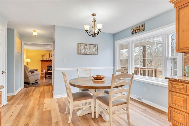 dining room featuring light wood finished floors, a brick fireplace, an inviting chandelier, and baseboards