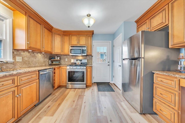 kitchen with appliances with stainless steel finishes, brown cabinetry, a sink, and light wood-style floors