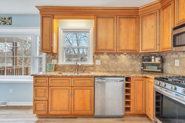 kitchen with appliances with stainless steel finishes, brown cabinets, a sink, and light stone counters