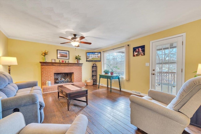 living area featuring visible vents, ceiling fan, hardwood / wood-style floors, crown molding, and a brick fireplace